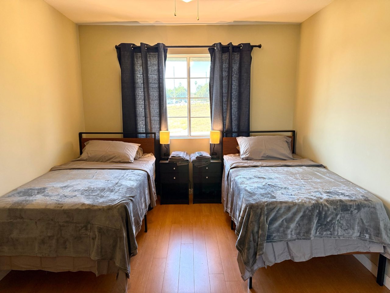 A bedroom with two made beds, bedside lamps and a bright window