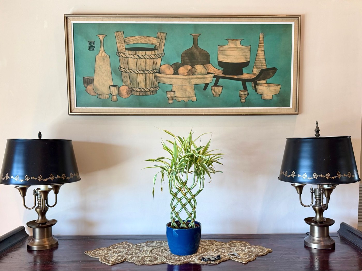 A console table at Path2 Recovery Center with a pair of brass lamps, a braided lucky bamboo plant and framed artwork